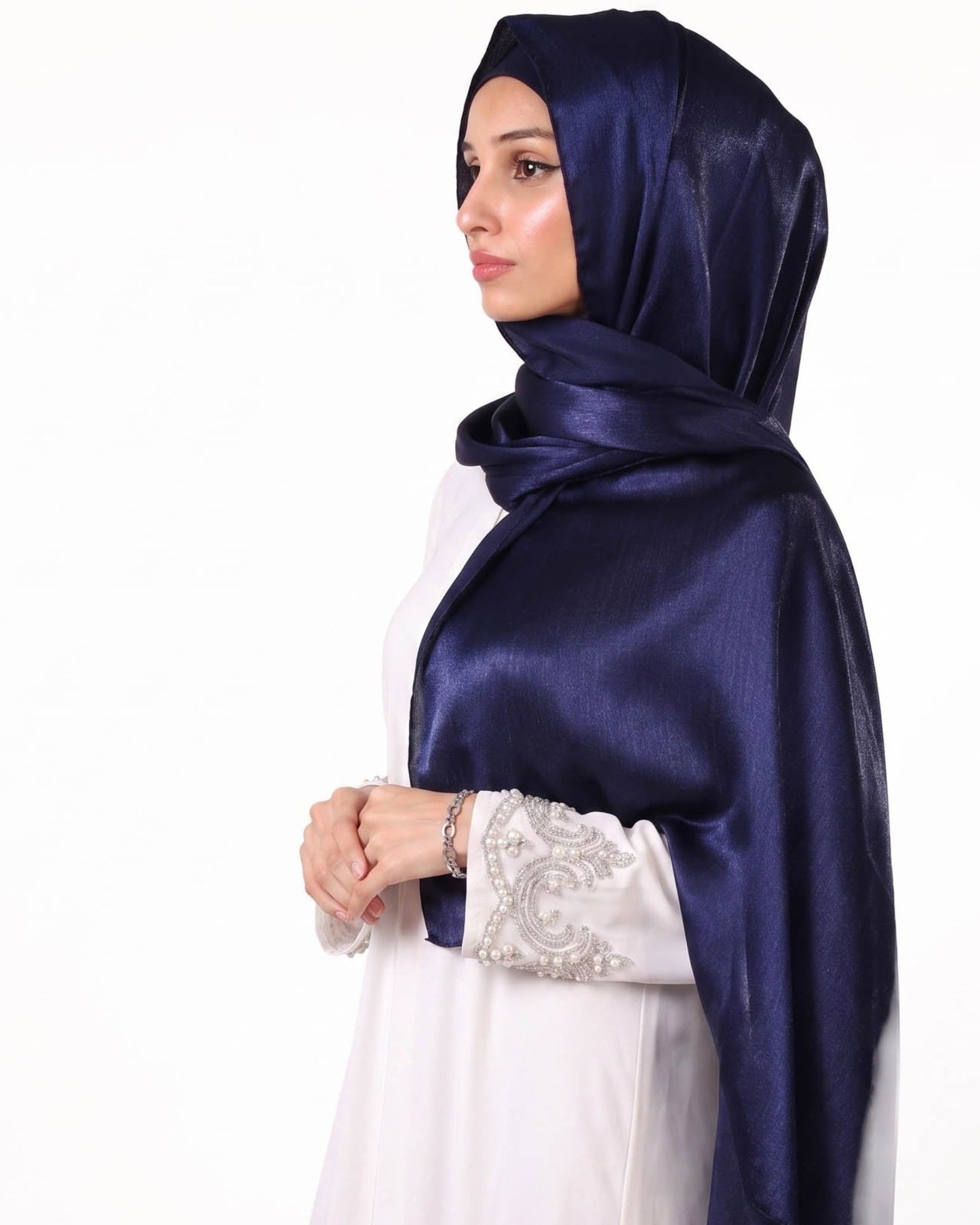 Woman wearing a navy blue hijab and white dress with lace details on a white background